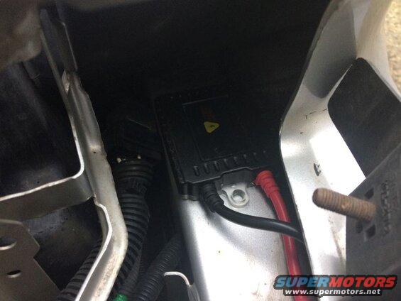Black ballast with red and black wires connected, mounted in a vehicle.