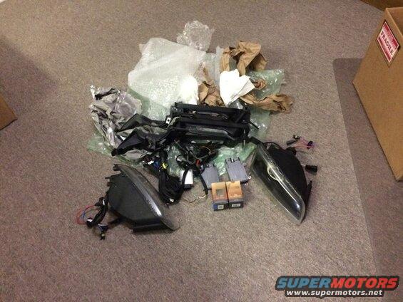 Car parts including headlights, wiring, and control modules on a carpeted floor.