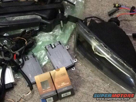 Automotive lighting parts including headlights, ballasts, and wiring harnesses on a carpeted surface.