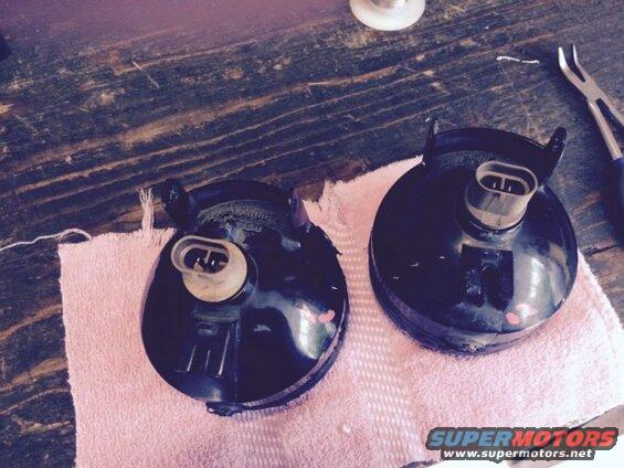 Two black fog light assemblies with electrical connectors on a pink towel.