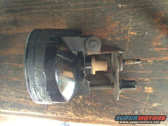 Black fog light assembly with metal brackets and springs on a wooden surface.