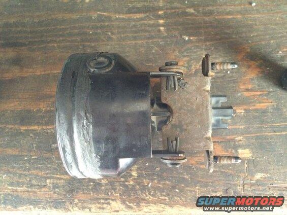 Black automotive light assembly with rusty bracket and screws on wood surface