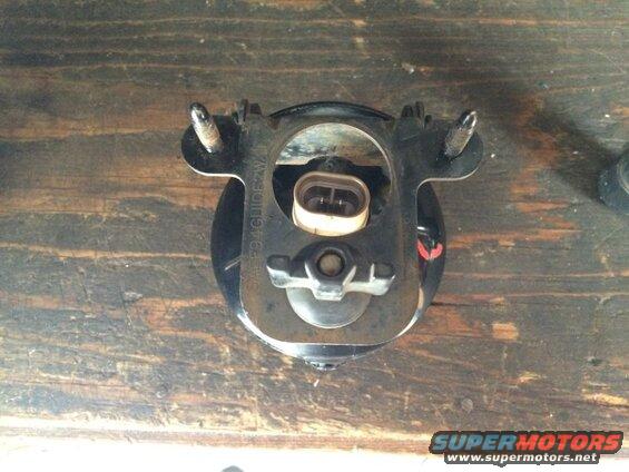 Automotive fog light assembly with metal bracket and electrical connector on a wooden surface.