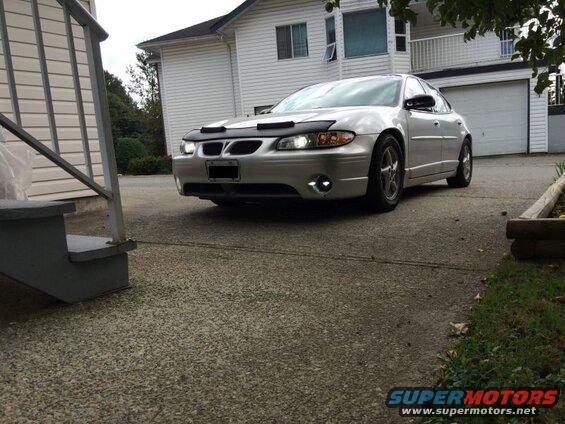 Silver Pontiac Grand Prix parked in driveway with headlights on.