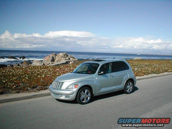 Silver 2004 Chrysler PT Cruiser parked on a road next to the ocean with rocks and flowers
