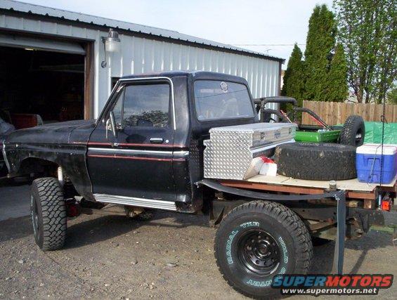 Black pickup truck with a flatbed, spare tire, toolbox, and cooler in the bed