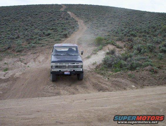 Black 1978 Ford Bronco driving up a dusty dirt hill with sagebrush on the sides