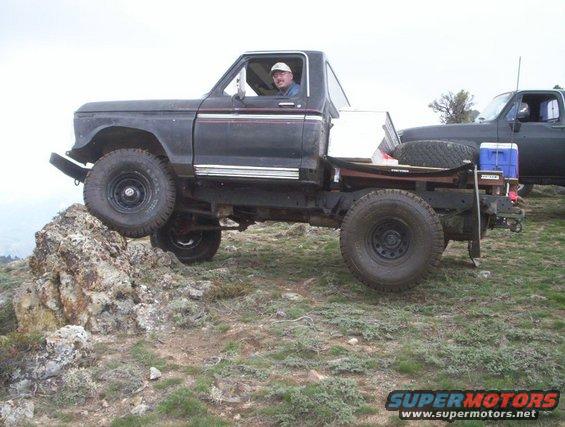 man driving a dark pickup truck with a flatbed, climbing over rocks off-road