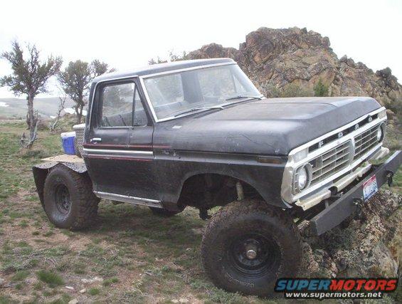 Black Ford F-Series truck with flatbed, lifted, off-road tires, on rocky terrain