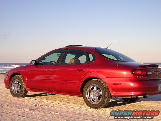 Red 1997 Ford Taurus parked on a sandy beach with the ocean in the background