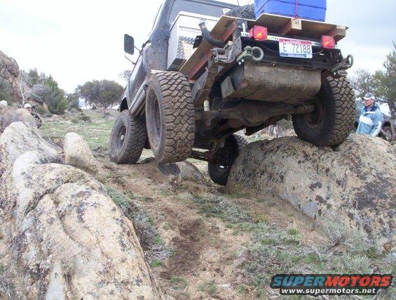 Off-road vehicle with large tires climbing over rocks, license plate E 72188 visible