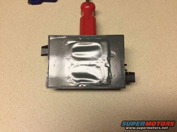 Black electronic module with shiny surface, red tool above, blue tool upper left.