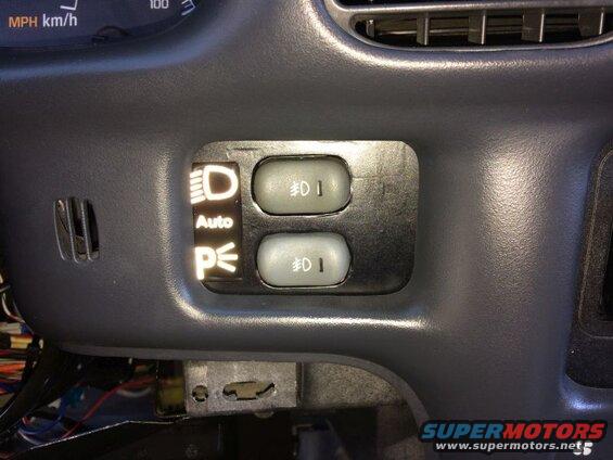 Car interior: illuminated headlight controls with symbols for headlights, auto, parking lights, and two fog light buttons.