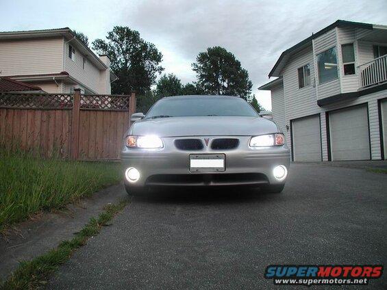 Silver 2002 Pontiac Grand Prix front view, headlights and fog lights on, parked in driveway.