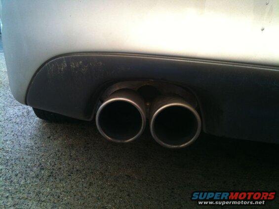 Dual exhaust pipes on a silver car with black bumper trim.