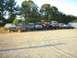 1989 Ford Bronco - Several SUVs and trucks are parked in a line on a gravel lot with trees in the background.