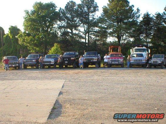 Several trucks and SUVs parked in a line, with people standing around them