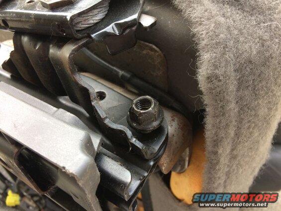 Close-up of vehicle seat adjustment bracket with nut and grey fabric.
