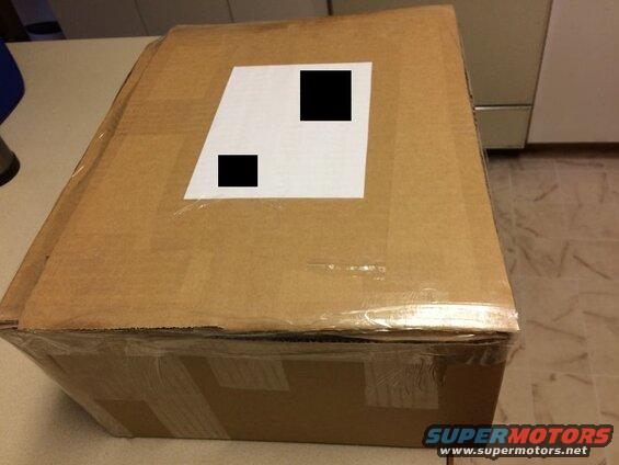 Cardboard box with a white label and black squares.
