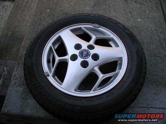 Silver Pontiac alloy wheel with black tire on concrete