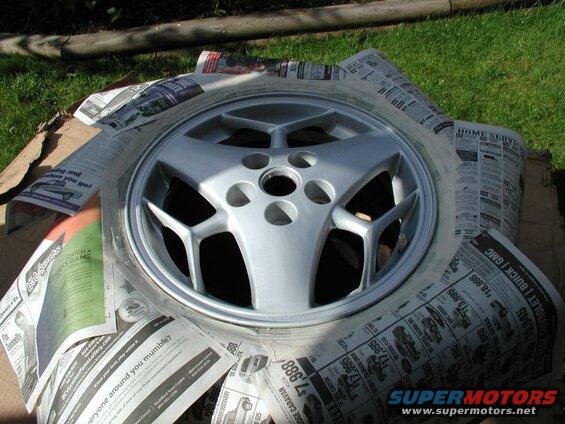 Silver five-spoke car wheel covered with newspapers, resting on cardboard.