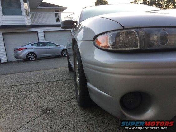 Front passenger side of a silver sedan, parked on a cracked asphalt driveway.