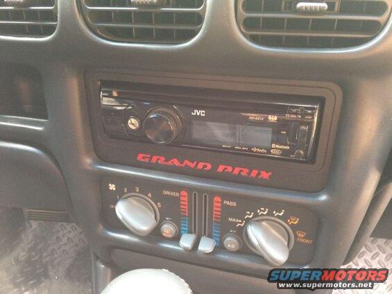 Car dashboard with JVC stereo and climate controls. Red "GRAND PRIX" text.