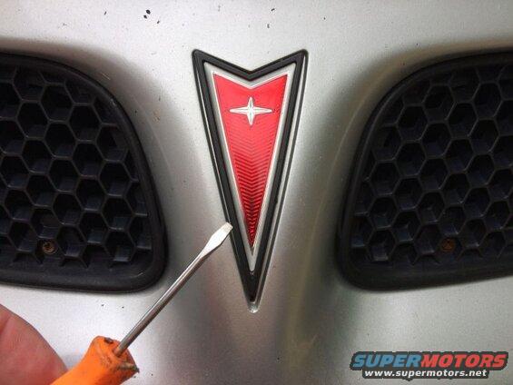Use a small flathead screwdriver and gently pry up the old emblem.