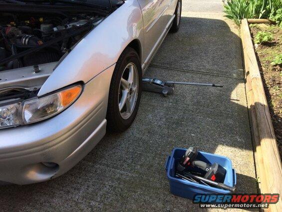 Silver Pontiac Grand Prix with hood open, car jack, and tools on driveway.