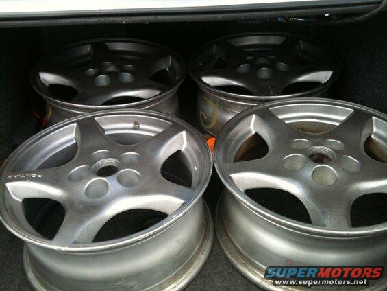 Four silver Pontiac Grand Prix wheels with five spokes in a vehicle trunk.