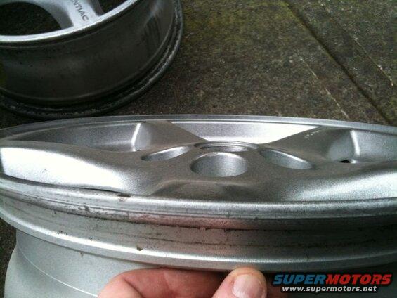 Close-up of two damaged silver alloy wheels, one in focus showing rim damage.