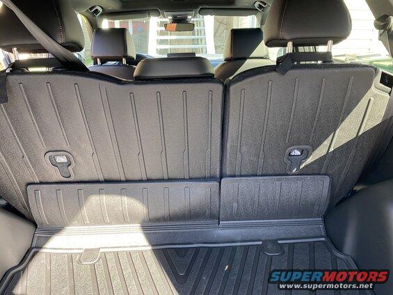 Back of folded rear seats in a vehicle cargo area with black protective mats.