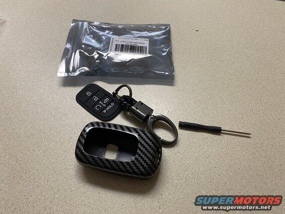 Carbon fiber key fob cover, key fob, screwdriver, and plastic package on a countertop.