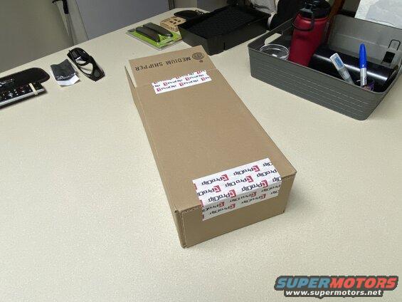 Cardboard box with ProClip tape on a table next to a storage bin with items.