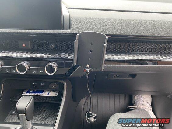 Car dashboard with phone mount, charging cable, gear shifter, and climate controls.