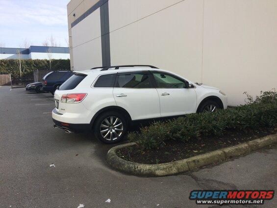 White Mazda CX-9 parked next to a building with bushes in front.