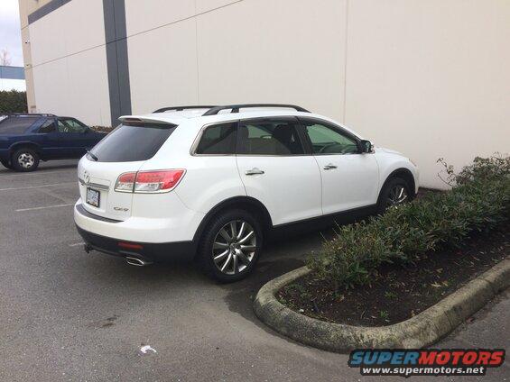 White 2009 Mazda CX-9 parked next to a building with a blue SUV in the background.