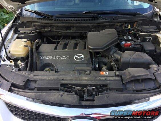 Engine bay of a Mazda CX-9, showing the V6 engine, battery, and air intake.