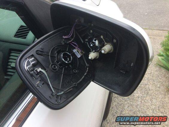 Close-up of a detached car side mirror assembly showing internal wiring and mounting components.