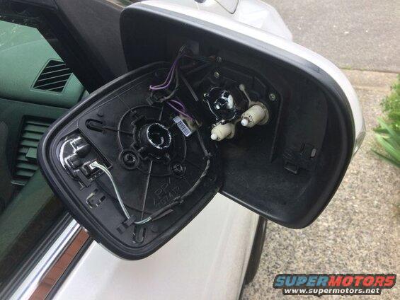 Back of a detached car side mirror assembly showing wires and internal parts.