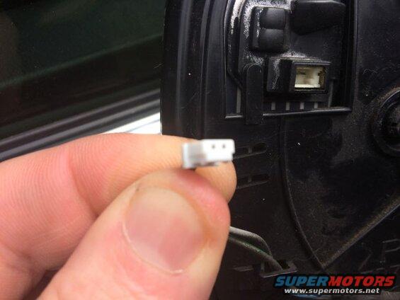 Close-up of a hand holding a white electrical connector near a black connector on a car mirror.