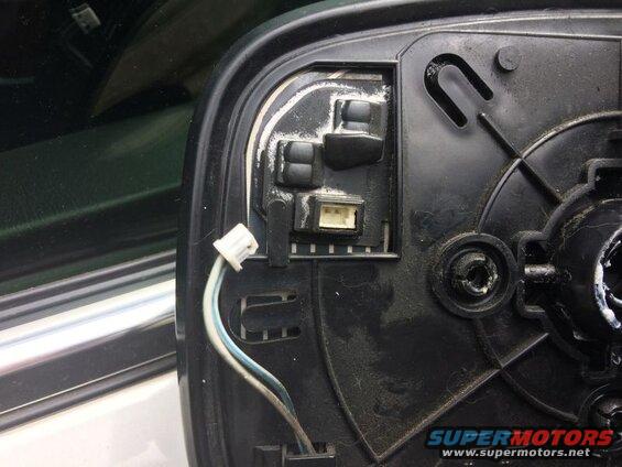 Back of a black plastic side mirror housing with an electrical connector and wires.