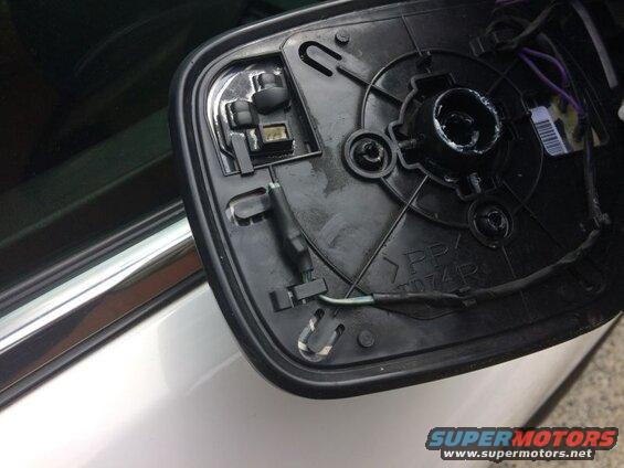 Back of a black side mirror assembly with wiring, mounting points, and part of a vehicle.