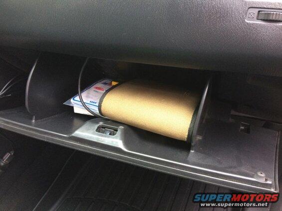 Open glove compartment in a car with a tan item and papers inside.