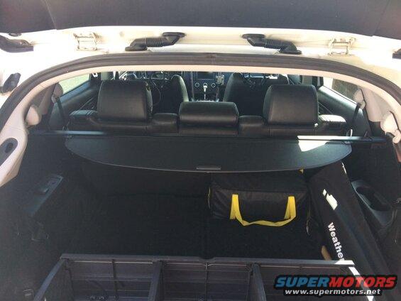 Interior of a white SUV cargo area with rear seats down, cargo cover extended, and storage bags.