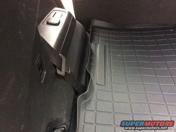 Interior cargo area of a vehicle with a rubber floor mat and storage compartment.