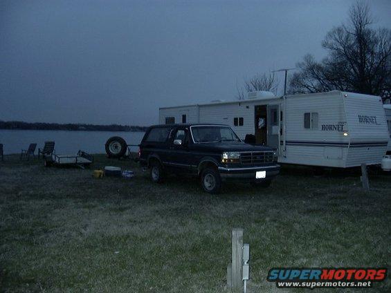 Dark blue Ford Bronco parked by a trailer near a lake