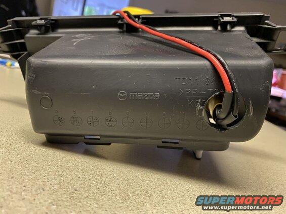 Black plastic automotive part with Mazda logo and wires