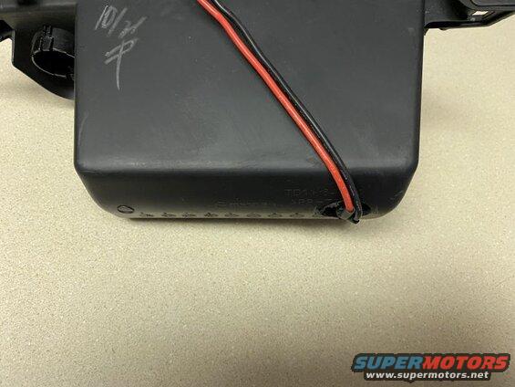Black plastic automotive part with red and black wires and embossed text.