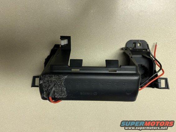 Black plastic automotive part with wires, featuring a Mazda logo.